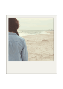 Frau wird zur Hälfte von hinten gezeigt und steht am Strand